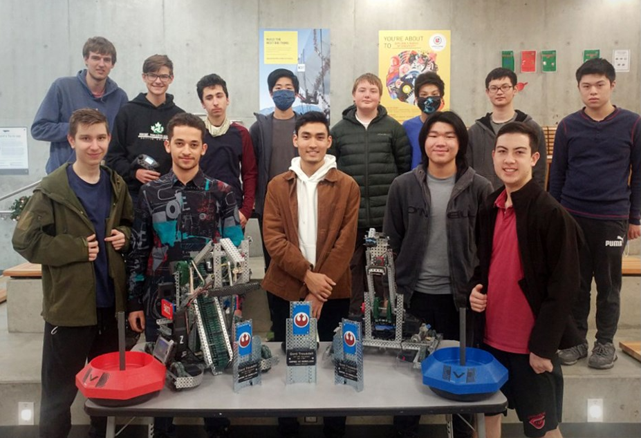 VEX robotics team photo with robots for 2nd place for alpha secondary — group of students posed behind two VEX robots and field elements.